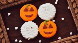 Dekorative Kürbisse und Halloween-Gebäck auf einem rustikalen Holzuntergrund arrangiert.