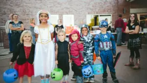 Eine Gruppe fröhlicher Kinder in Halloween-Kostümen sammelt Süßigkeiten bei einem abendlichen Rundgang.