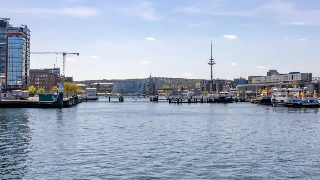 Blick auf das Kieler Hafenbecken mit modernen Gebäuden und dem markanten Fernsehturm im Hintergrund.