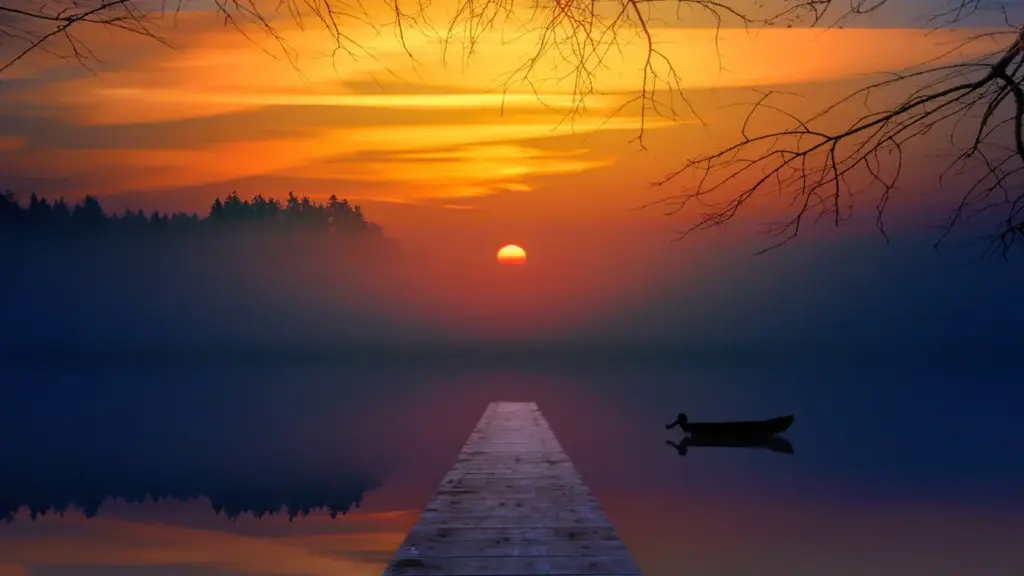 Ein hölzerner Steg führt in einen nebligen, ruhigen See bei Sonnenaufgang.